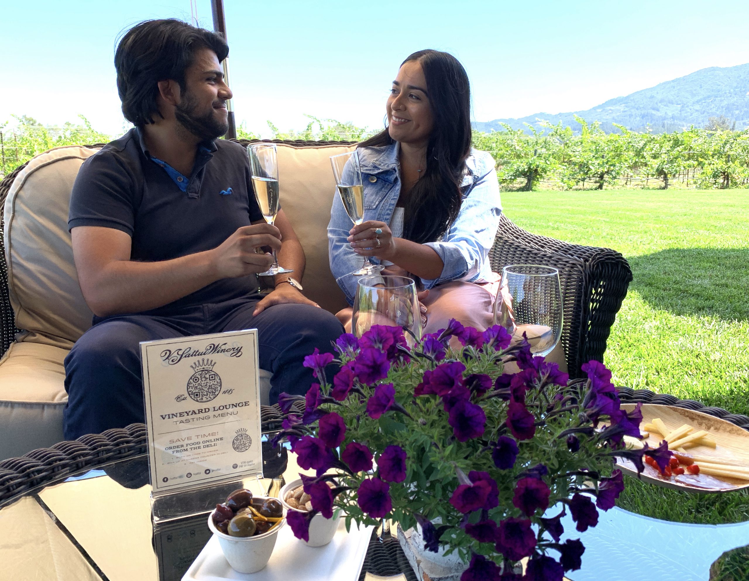 a man and woman sitting at a table with flowers and a sign