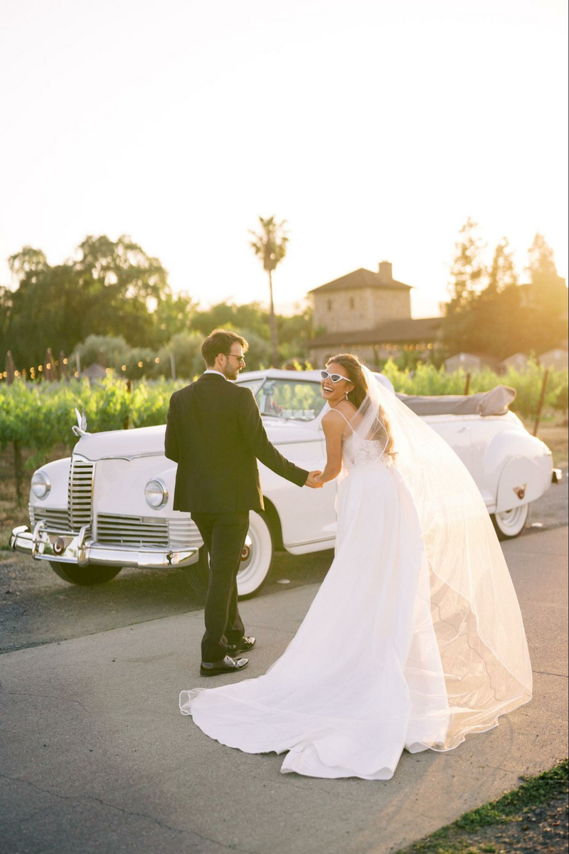 a bride and groom holding hands in front of a vintage car